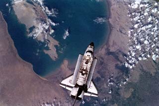 View of the space shuttle Atlantis, STS-71 mission, with a cloudy earth as a background. The payload bay is open as Atlantis makes preparations to dock with the Mir space station.